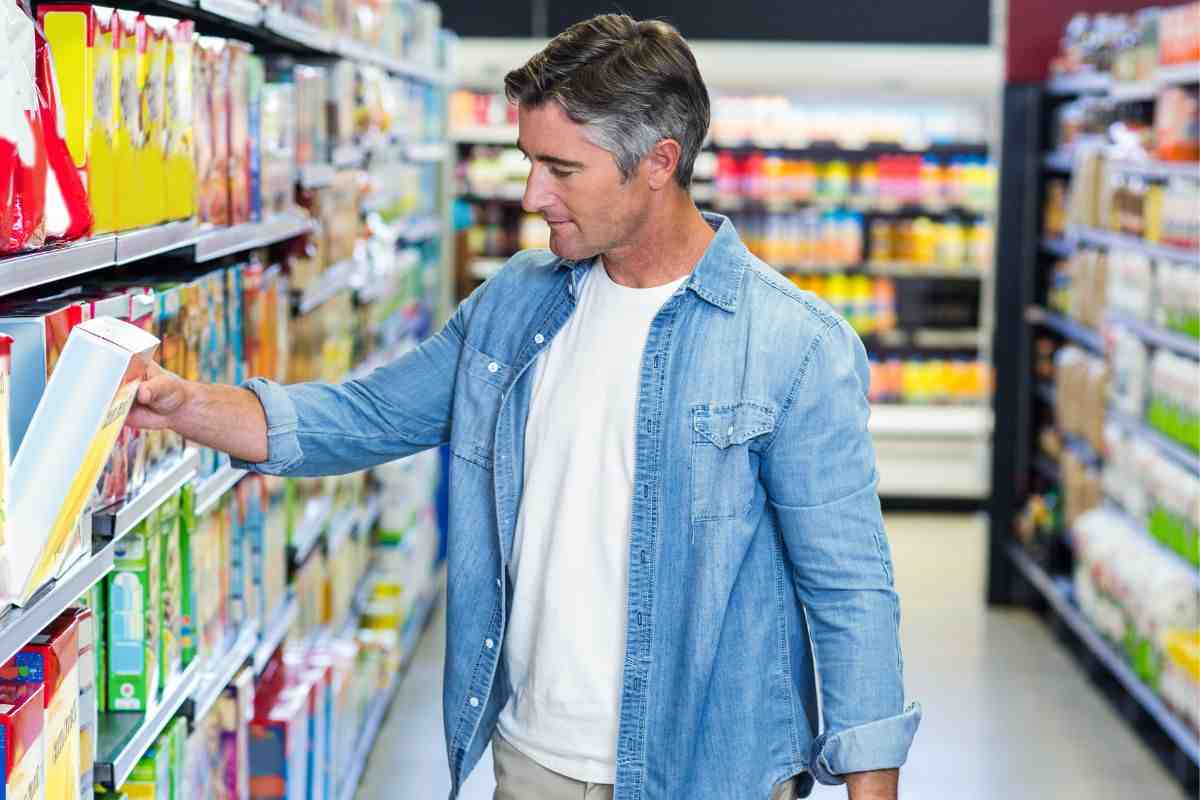 uomo che prende una scatola di cereali dallo scaffale di un supermercato